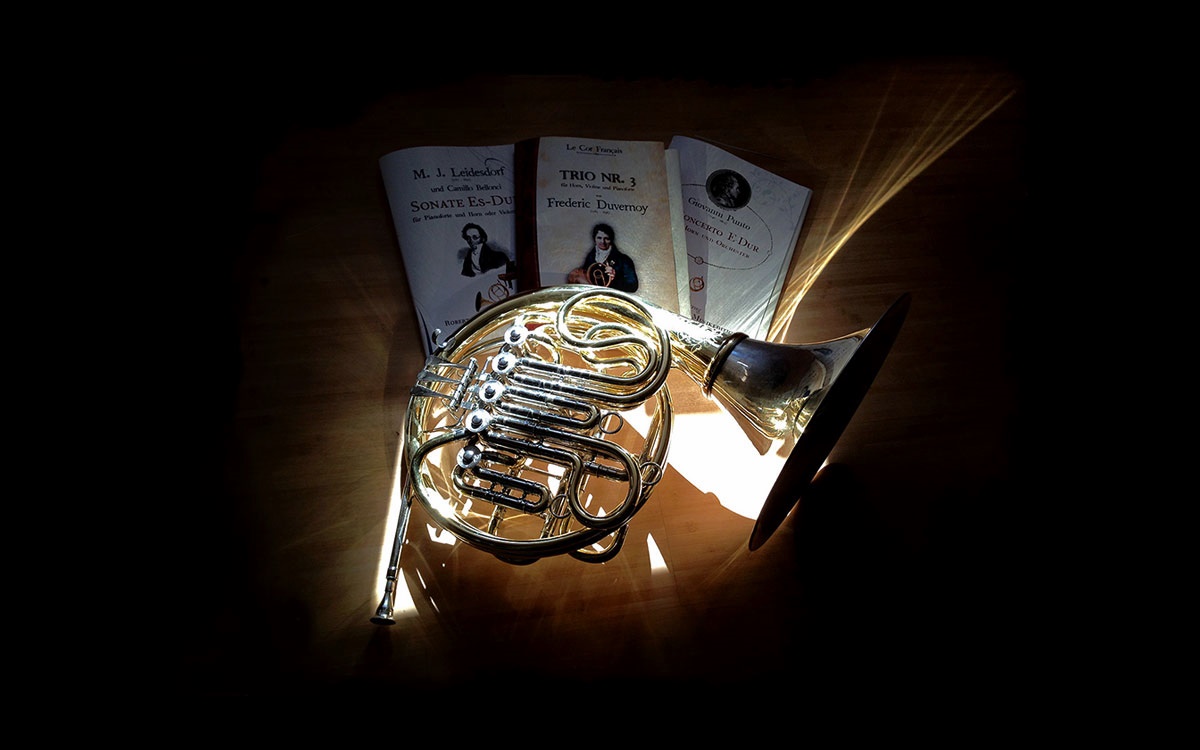 A French horn resting on sheet music for horn compositions
